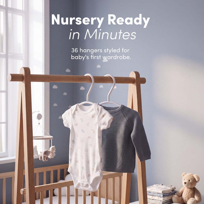 Baby bodysuit and jumper hanging on white nursery hangers in a nursery