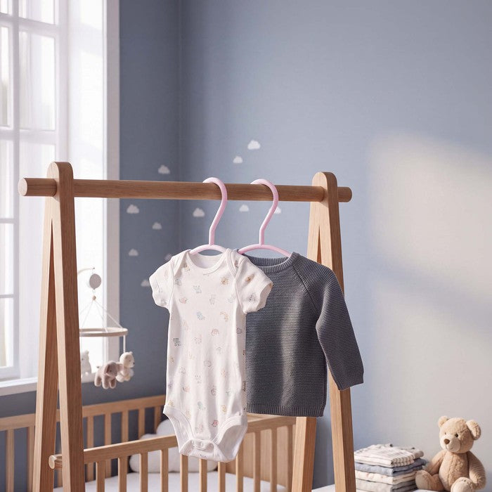 Pink nursery hangers holding a baby bodysuit and grey jumper on a clothes rail