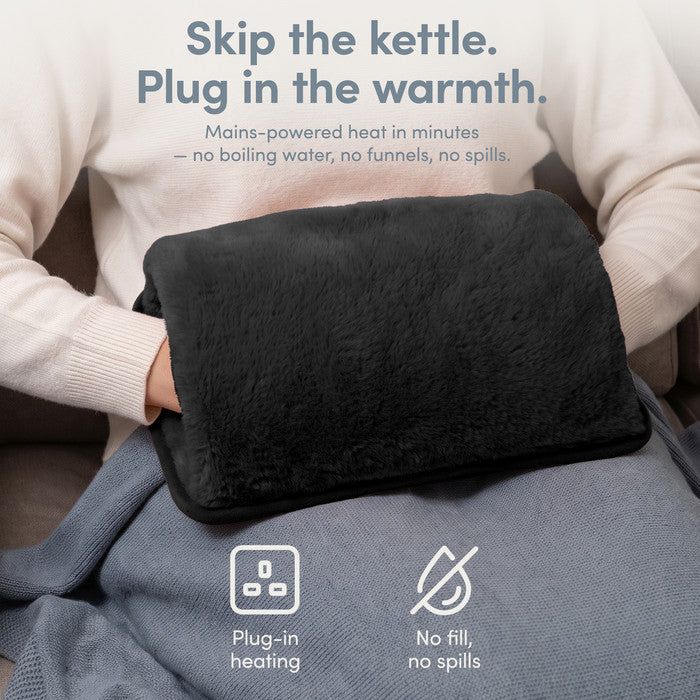 Black rechargeable hot water bottle on lap, plug-in heat with no filling or spills