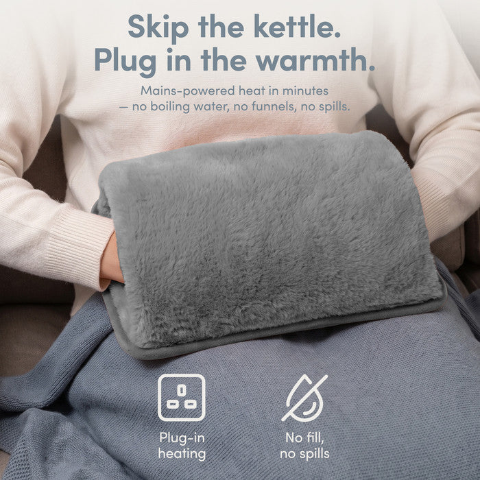 Grey rechargeable hot water bottle on lap, plug-in heat with no filling or spills