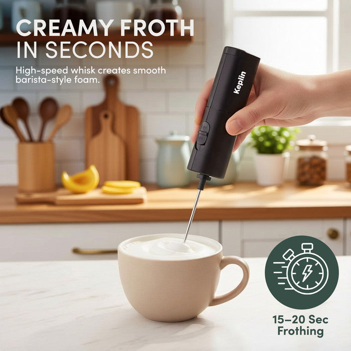 Hand holding slim milk frother over cup of creamy frothed milk in kitchen