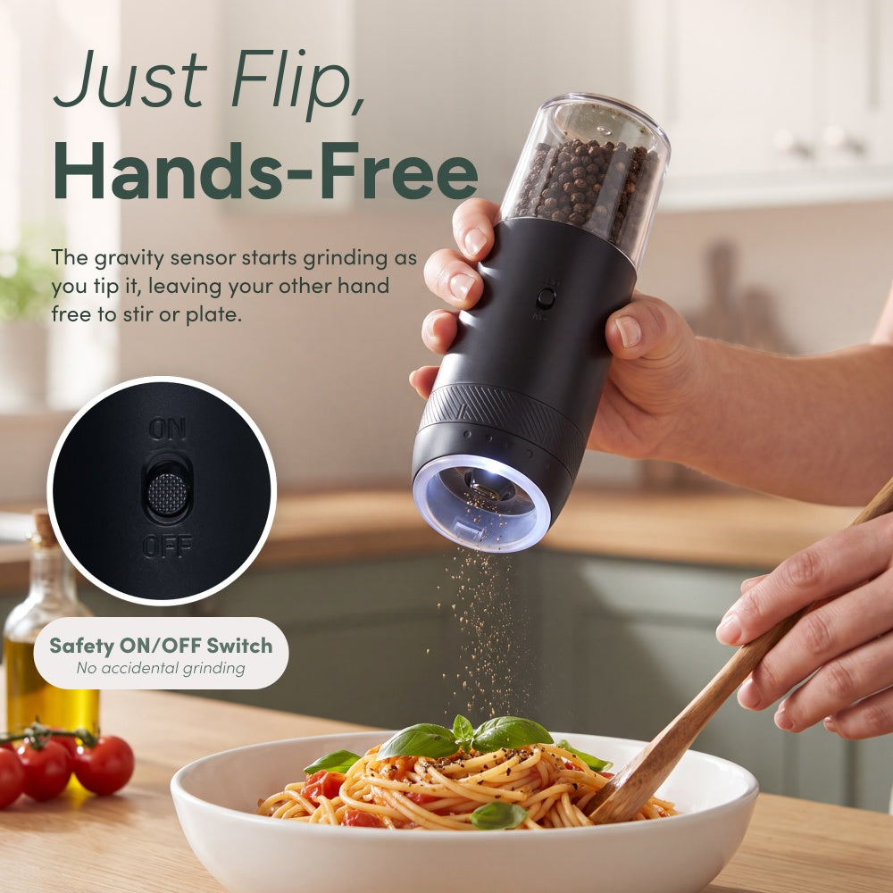 Hand tipping a black gravity mill to grind pepper onto pasta with the ON/OFF safety switch in close-up