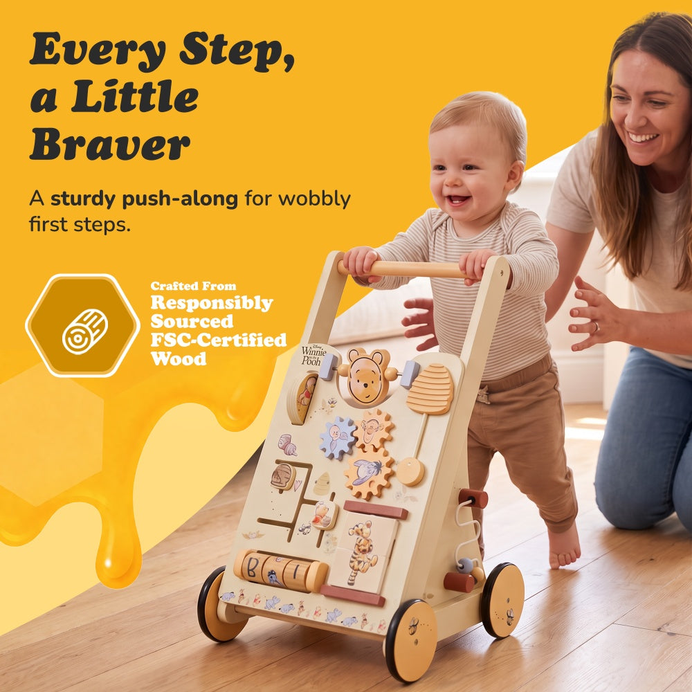 Toddler taking first steps with the Winnie the Pooh wooden push-along walker and a smiling parent nearby