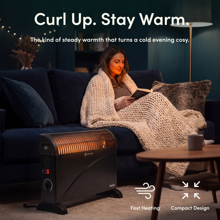 Black convector heater warming living room while woman reads under a blanket