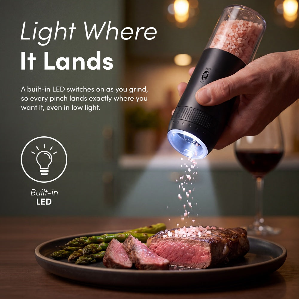 Black gravity mill with built-in LED lighting pink salt falling onto sliced steak and asparagus