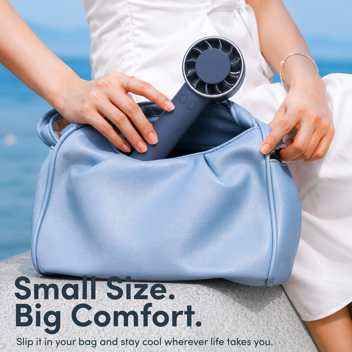 Midnight blue mini portable fan being placed into handbag – compact travel size