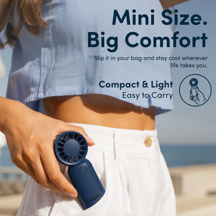 Woman at beach holding KEPLIN small handheld fan showing compact pocket size for travel and holidays
