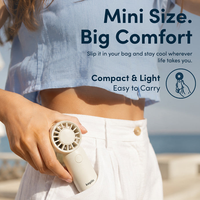 Woman at beach holding KEPLIN small handheld fan showing compact pocket size for travel and holidays