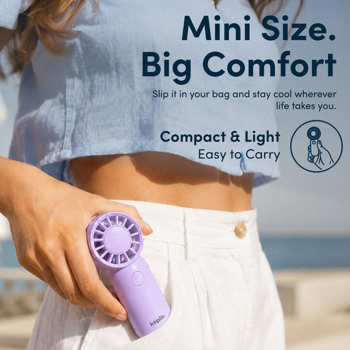 Woman at beach holding KEPLIN small handheld fan showing compact pocket size for travel and holidays