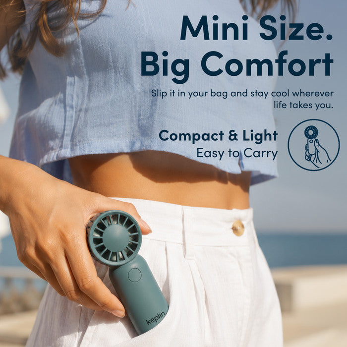 Woman at beach holding KEPLIN small handheld fan showing compact pocket size for travel and holidays