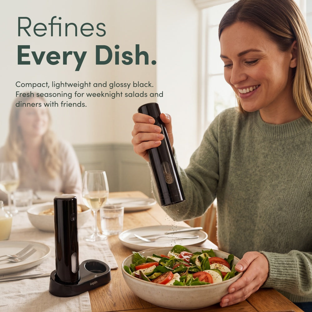 Woman seasoning a salad bowl with a black rechargeable mill at a dining table while a second mill sits on its base