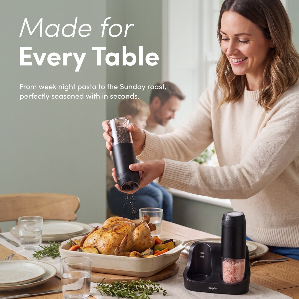 Woman grinding pepper from a black gravity mill over a roast chicken dinner with the other mill on its base