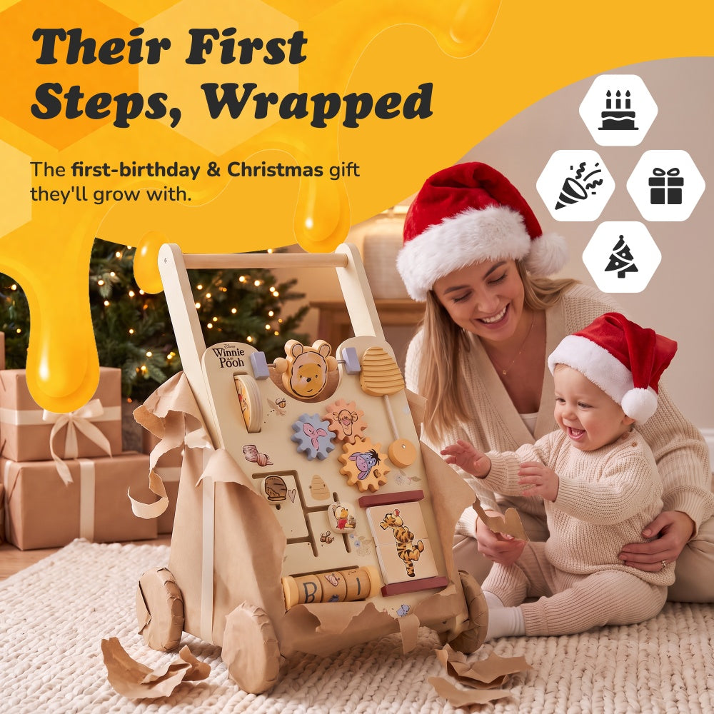Baby in a Santa hat unwrapping the Winnie the Pooh wooden walker from brown paper beside a parent