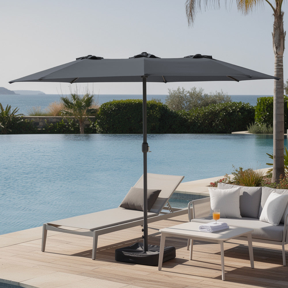 Grey double garden parasol open over modern outdoor sofa set on a patio with lush garden