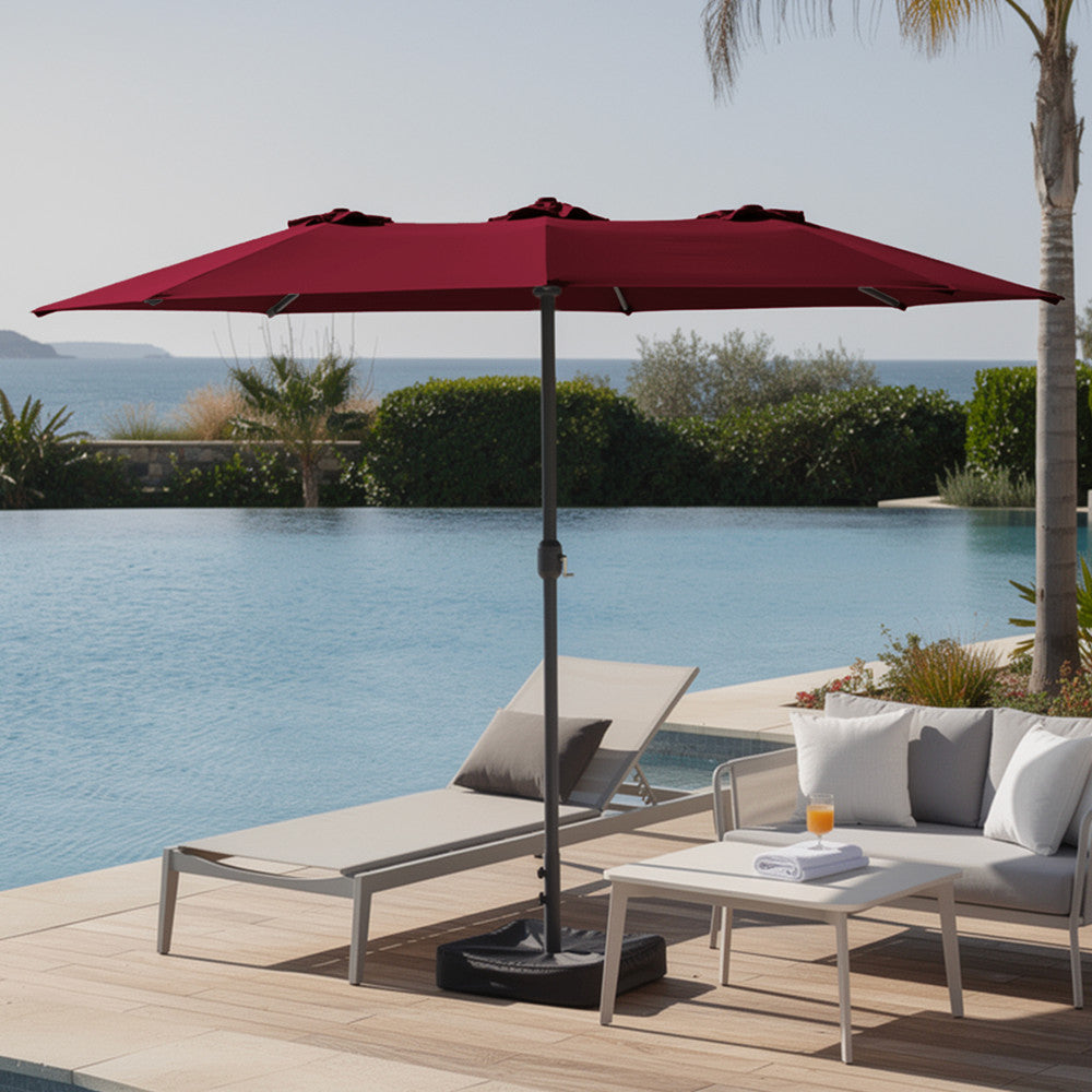 Red double garden parasol open over modern outdoor sofa set on a patio with lush garden