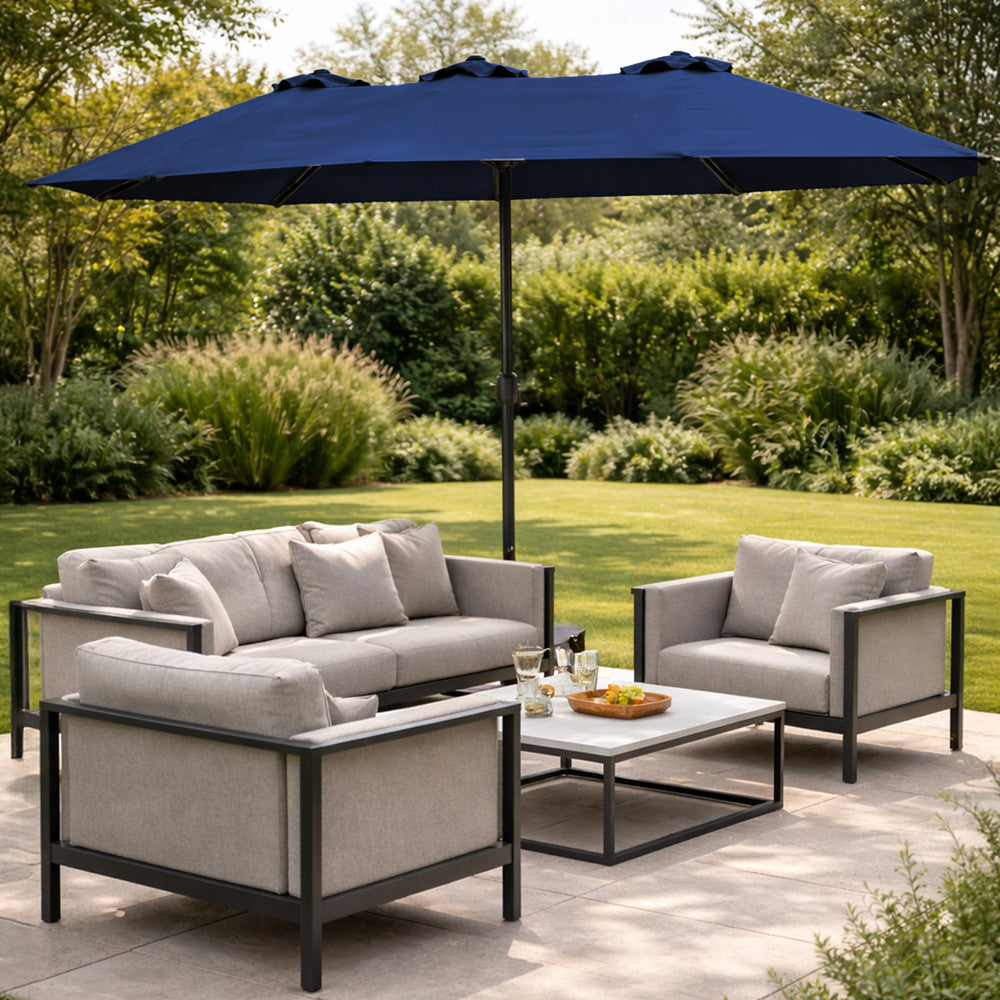Blue double garden parasol open over modern outdoor sofa set on a patio with lush garden